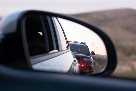 A right side mirror shows the reflection of a police car with its lights on.