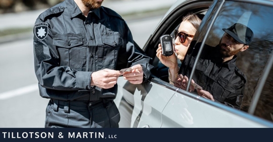woman in car blowing into breathalyzer while police officer stands and looks at her ID